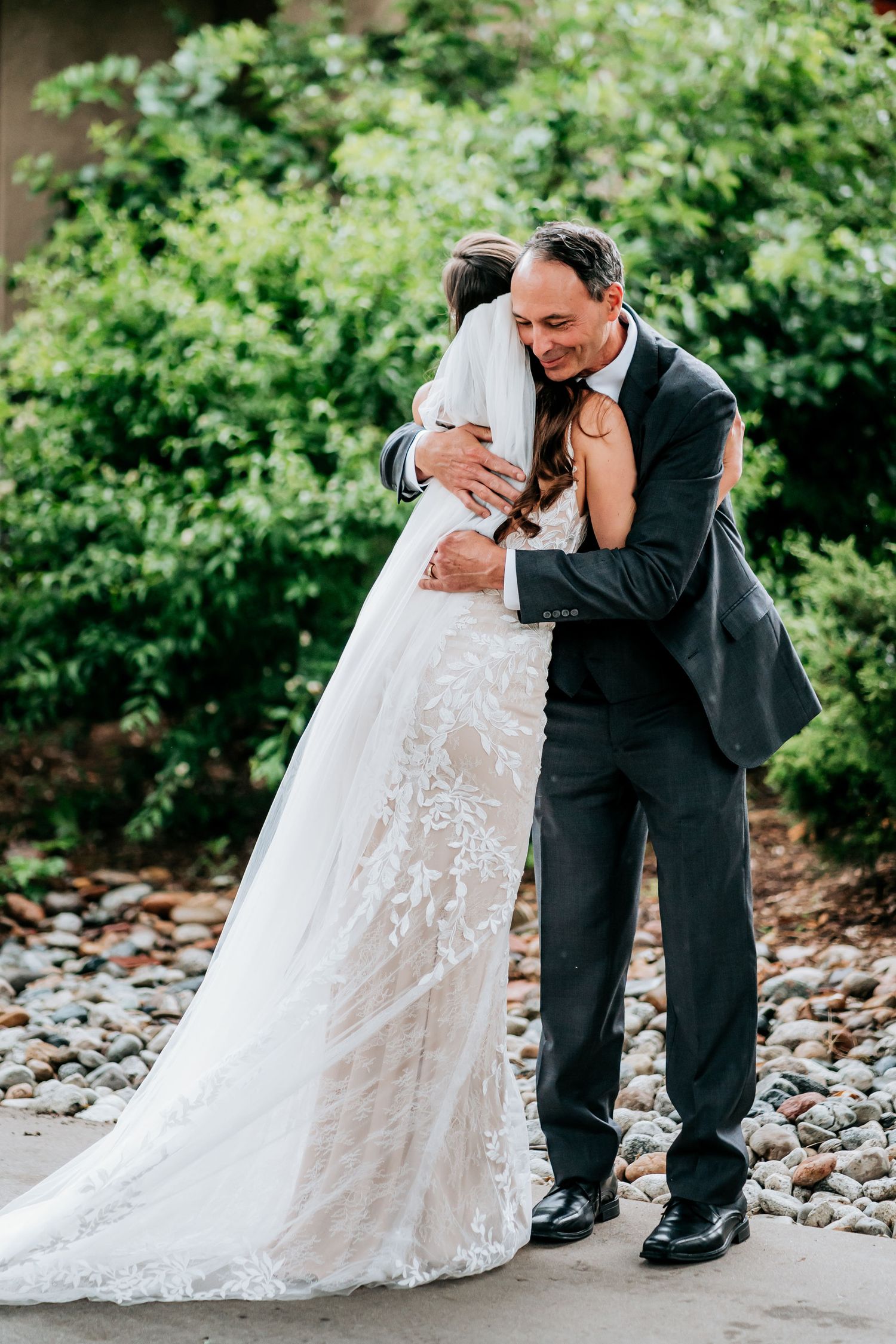 A tender moment captured between newlyweds embracing outdoors against lush greenery.