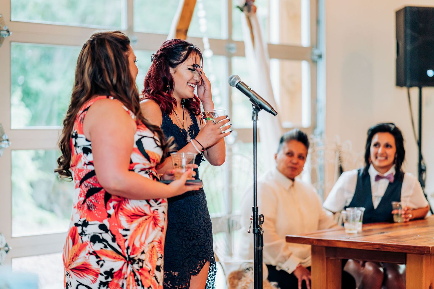 Two people perform a duet at a microphone during a wedding reception as guests watch from a table.