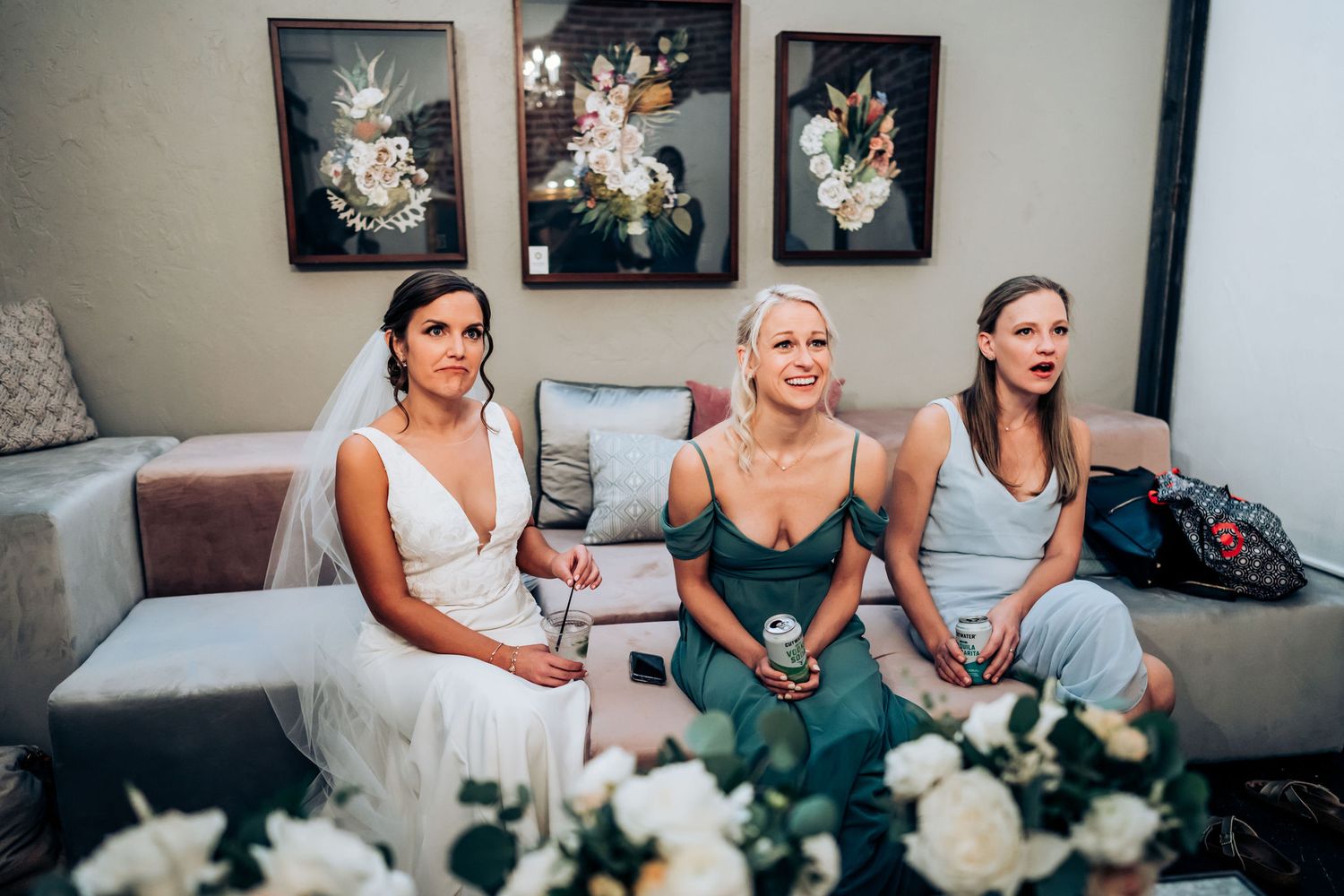 Three people sitting on a couch with floral artwork and white bouquets.