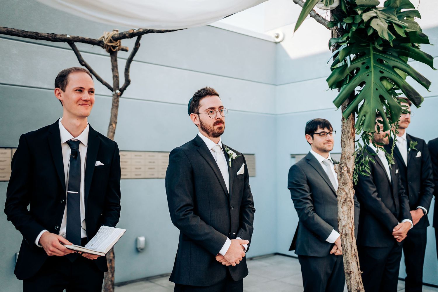 Groomsmen in suits stand together at a modern indoor wedding venue.