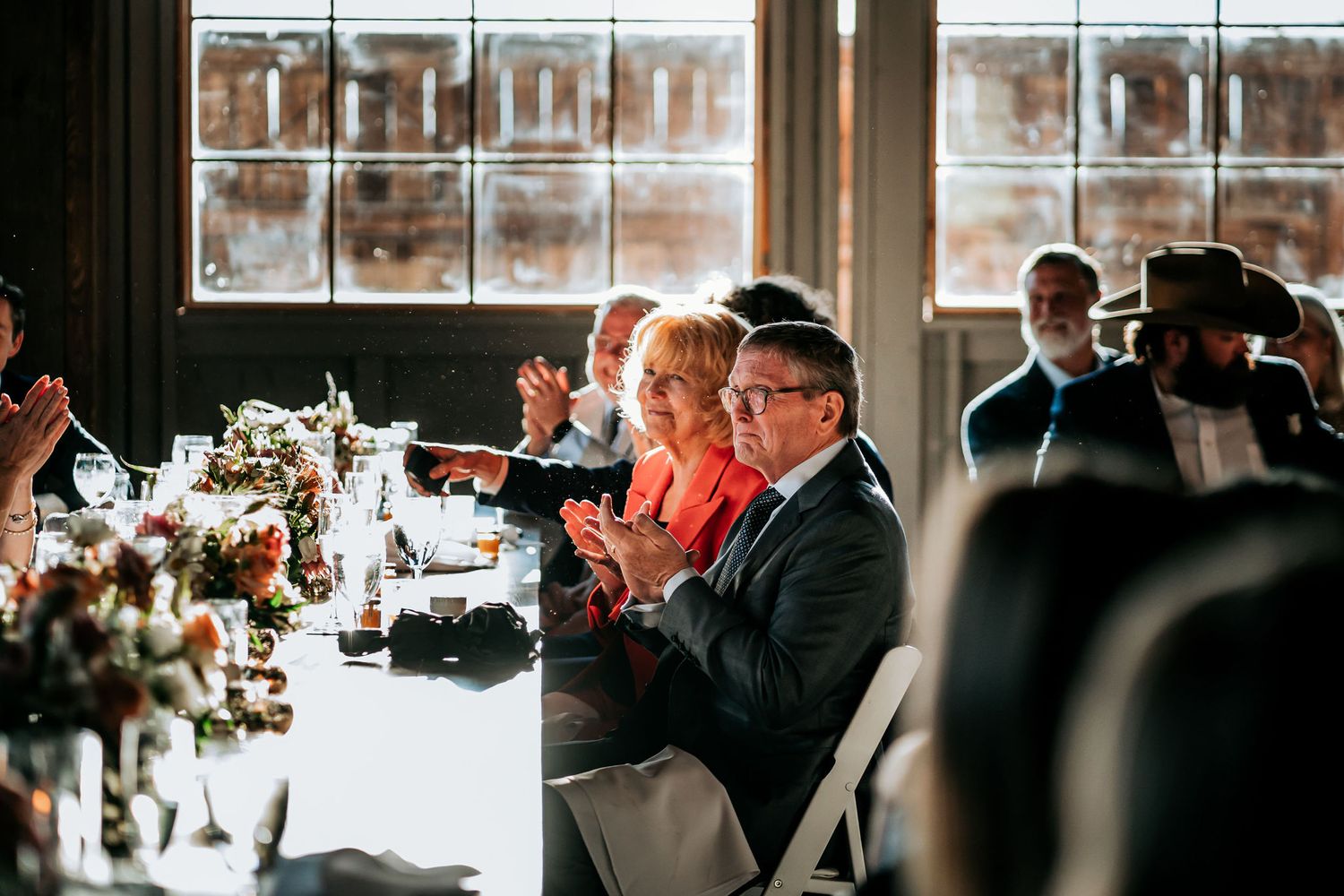 Wedding guests enjoy dinner at a beautifully decorated table with floral centerpieces.