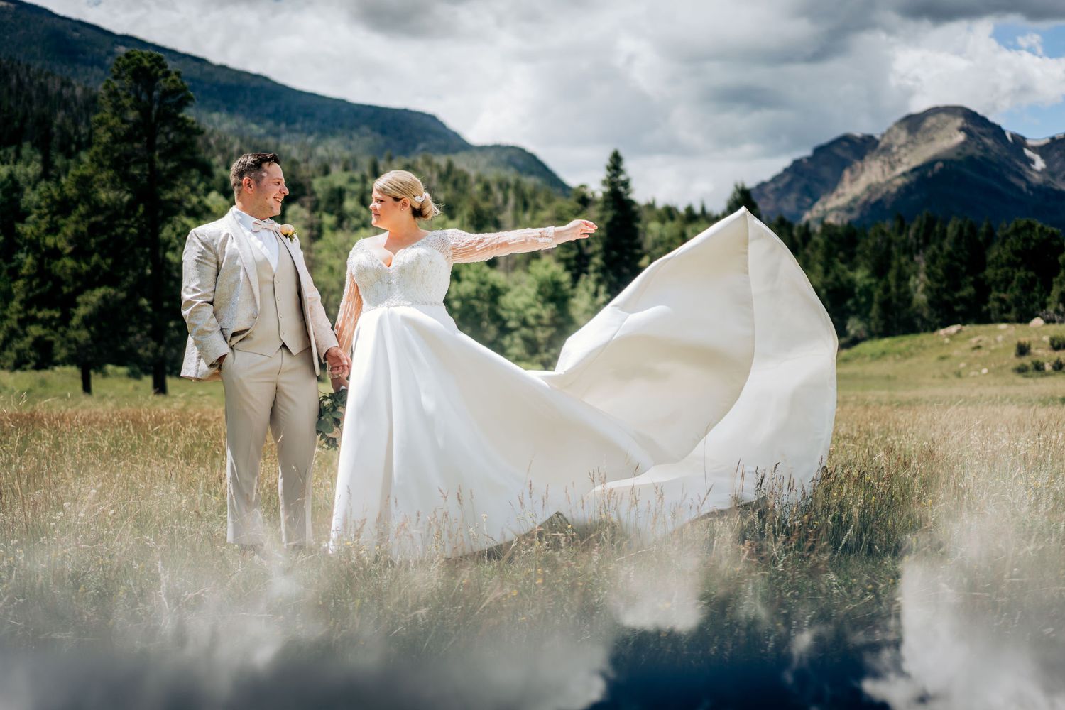 Wedding couple in an alpine meadow with flowing white dress against mountain landscape.
