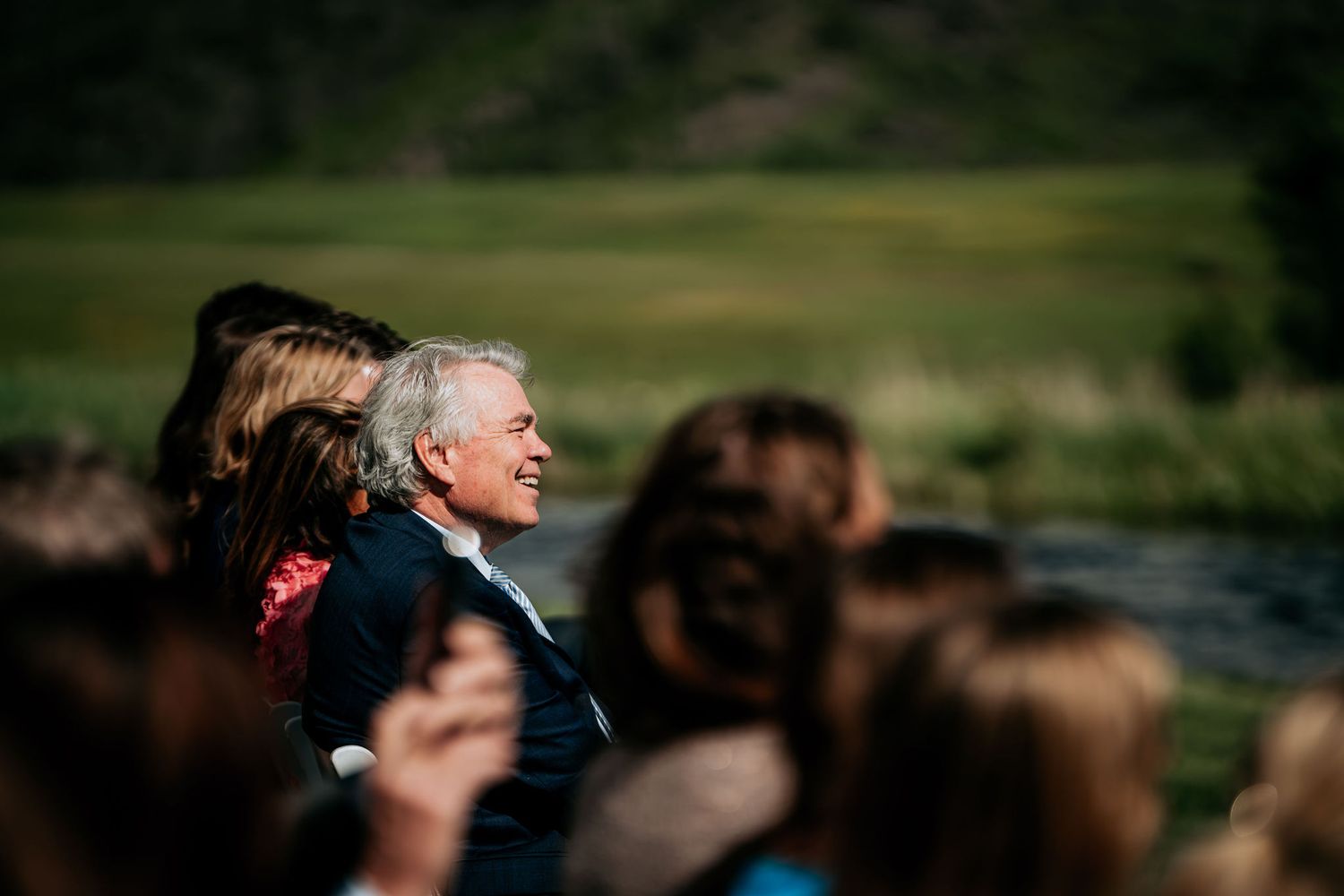 Guest watches outdoor mountain wedding ceremony with joyful expression.