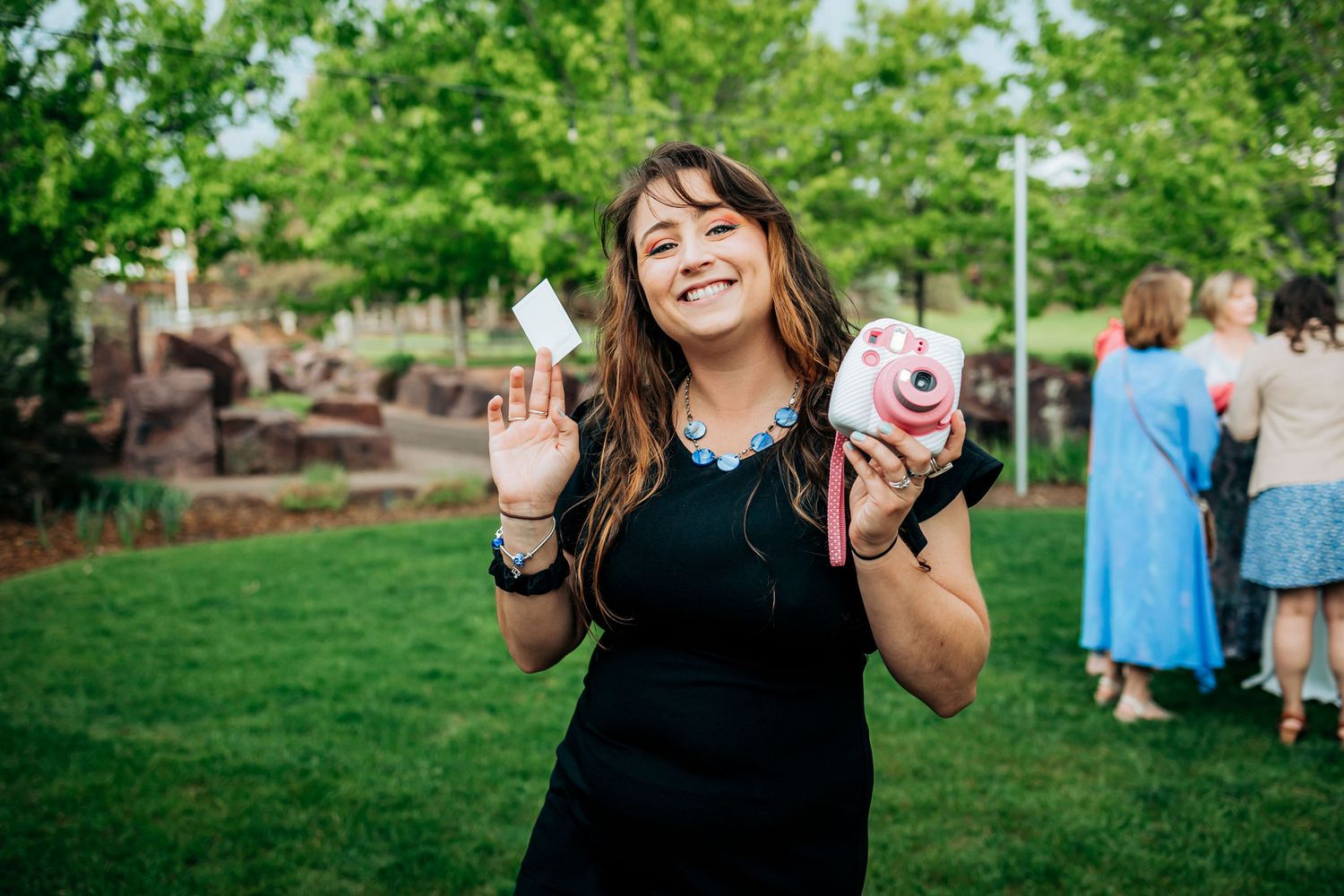 Wedding guest in black dress enjoying celebratory drinks at outdoor reception.