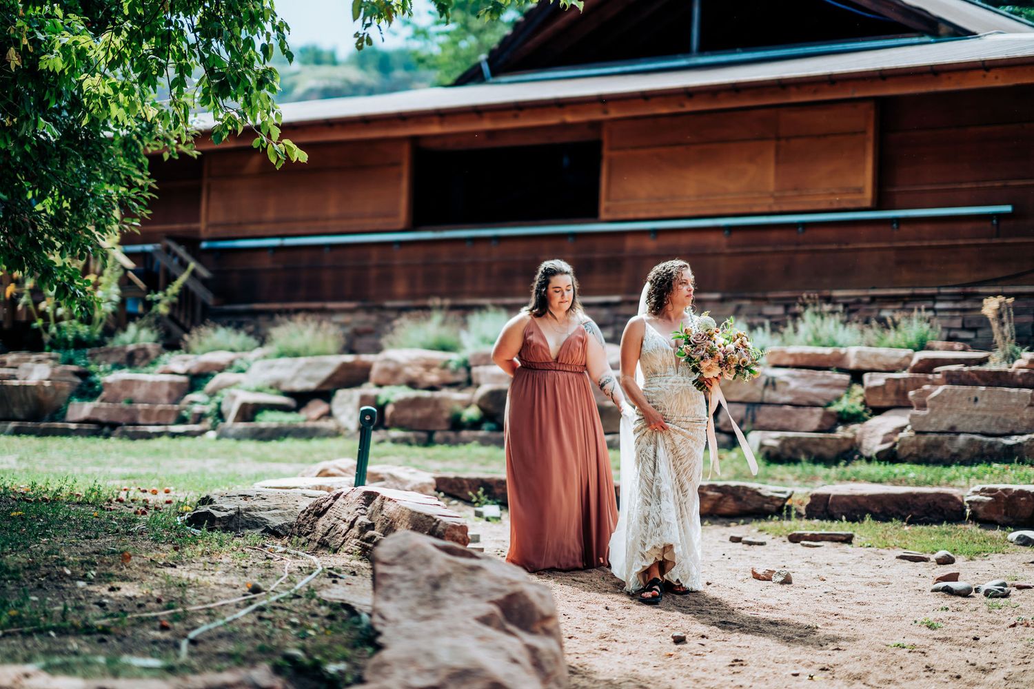 Two people walking together outdoors near a rustic wooden building on a sunny day.