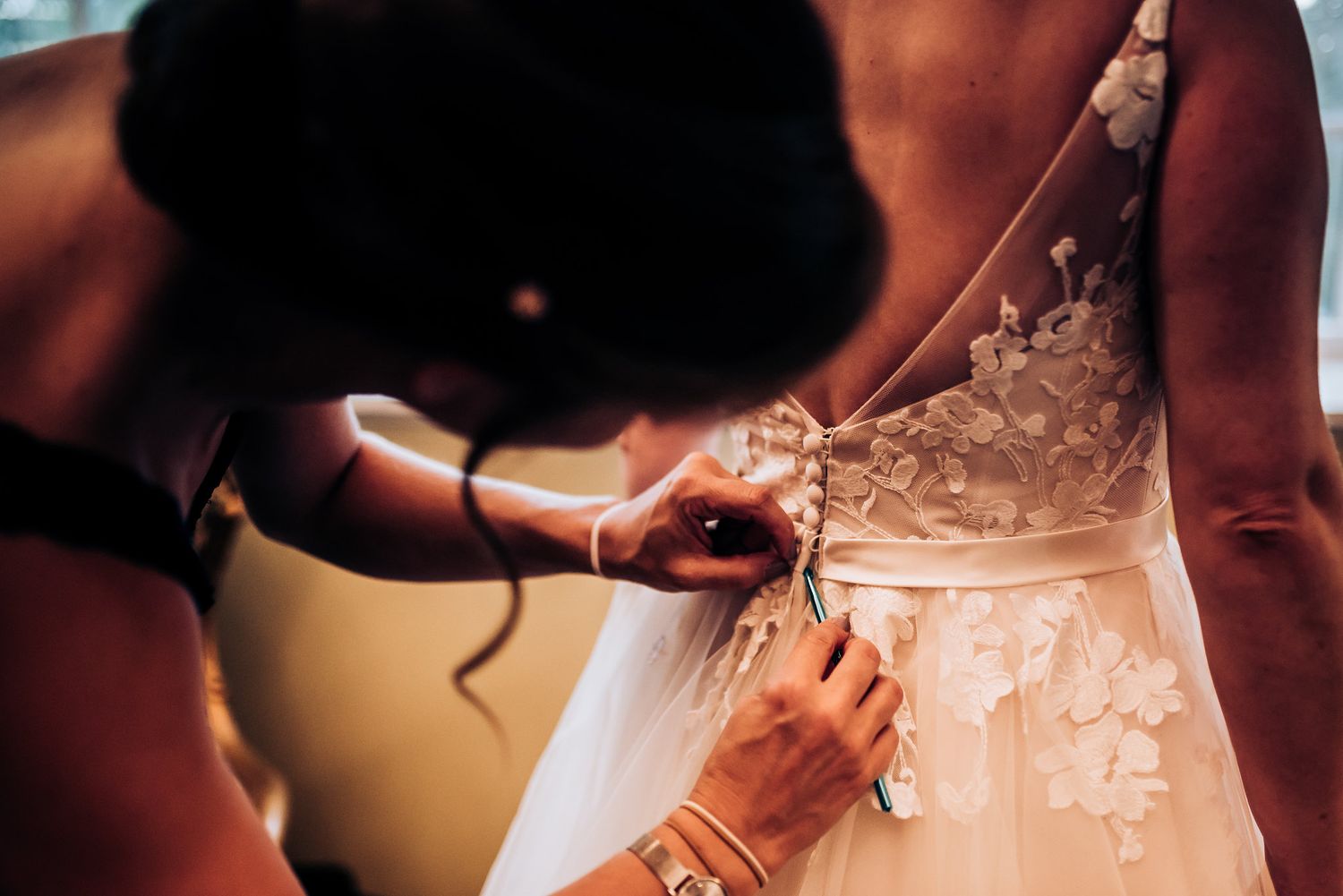 Close-up of hands adjusting the back of a detailed lace wedding dress.