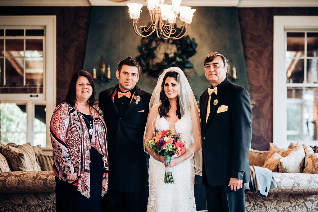 Formal wedding portrait in an elegant room with dark walls and chandelier overhead.