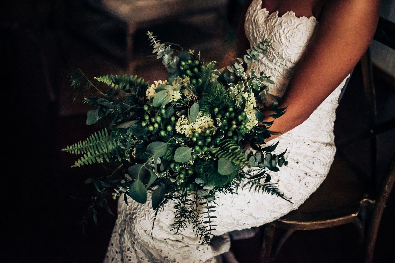 Close-up of wedding bouquet with white dress featuring green foliage and ferns.