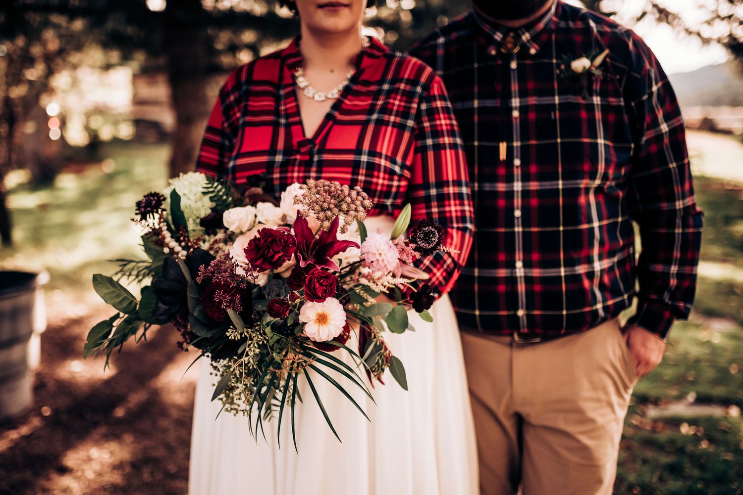 Close-up of burgundy and pink floral bouquet with plaid and white attire visible.