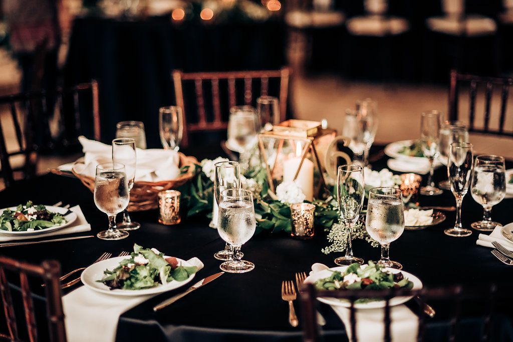 Formal wedding reception table setting with elegant place settings, wine glasses and fresh green salads.