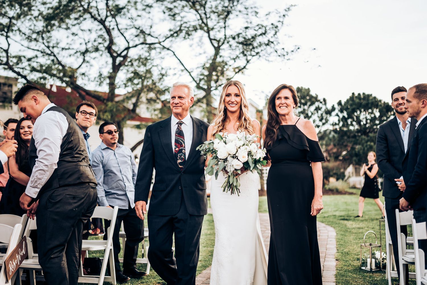 Wedding party gathered on green lawn during outdoor ceremony.