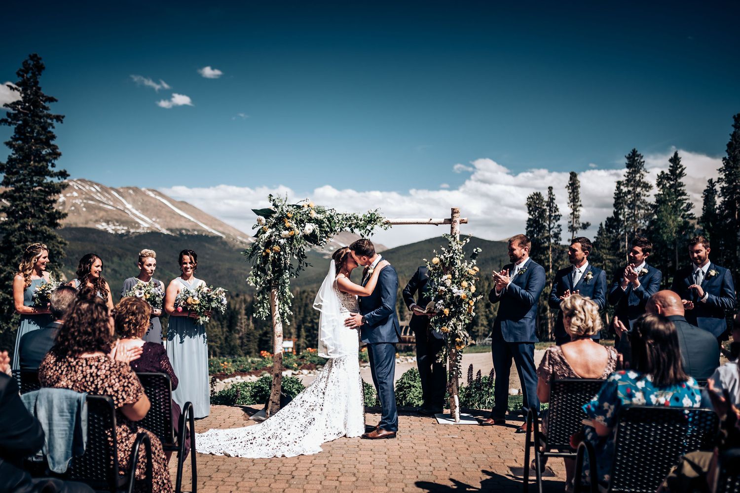Wedding ceremony overlooking mountain landscape with guests seated on rustic chairs.