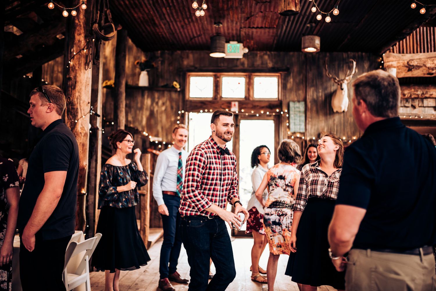 People mingling inside a wooden barn venue with string lights overhead.