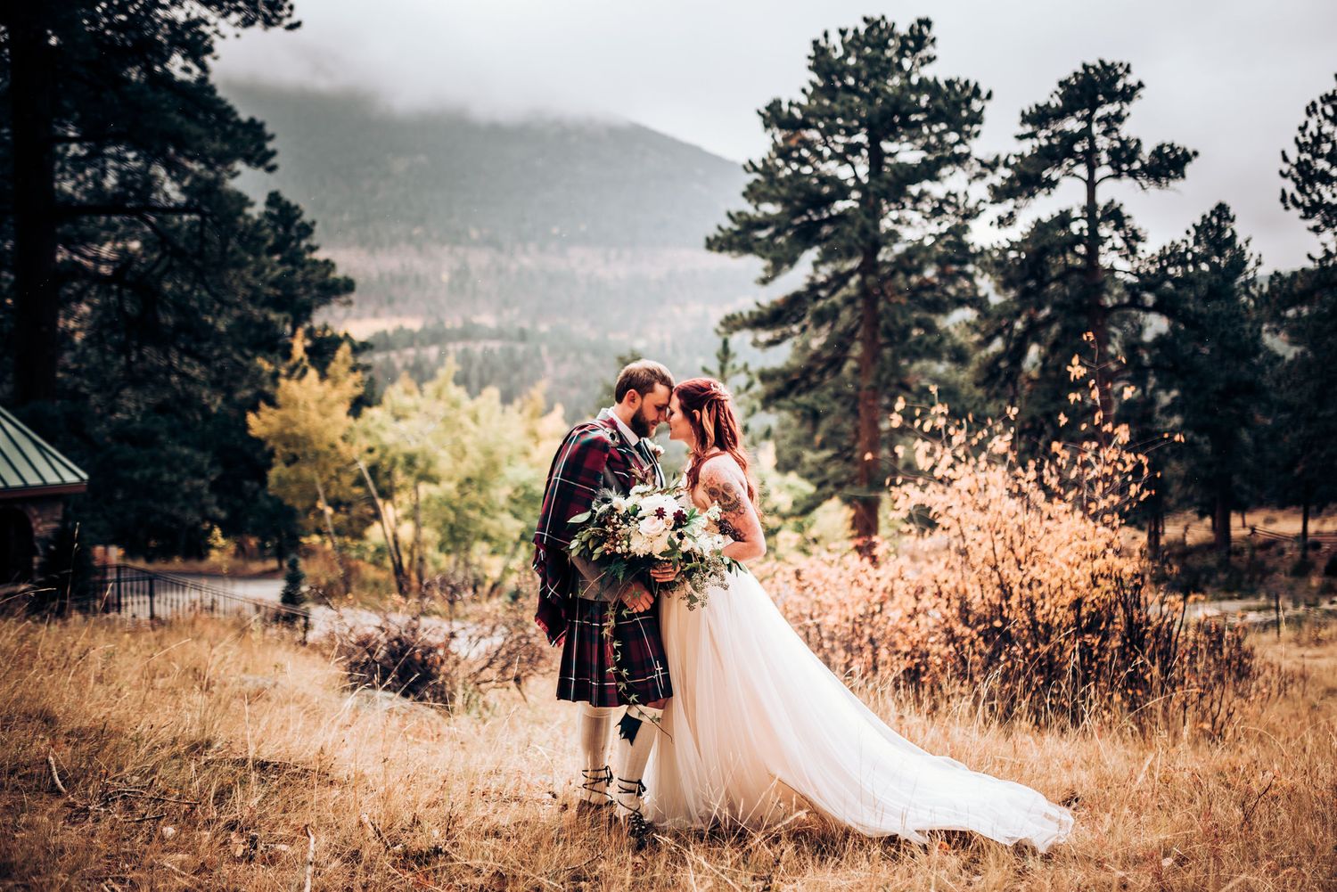 Wedding couple embraces on mountainside in Scottish wedding attire during golden hour.