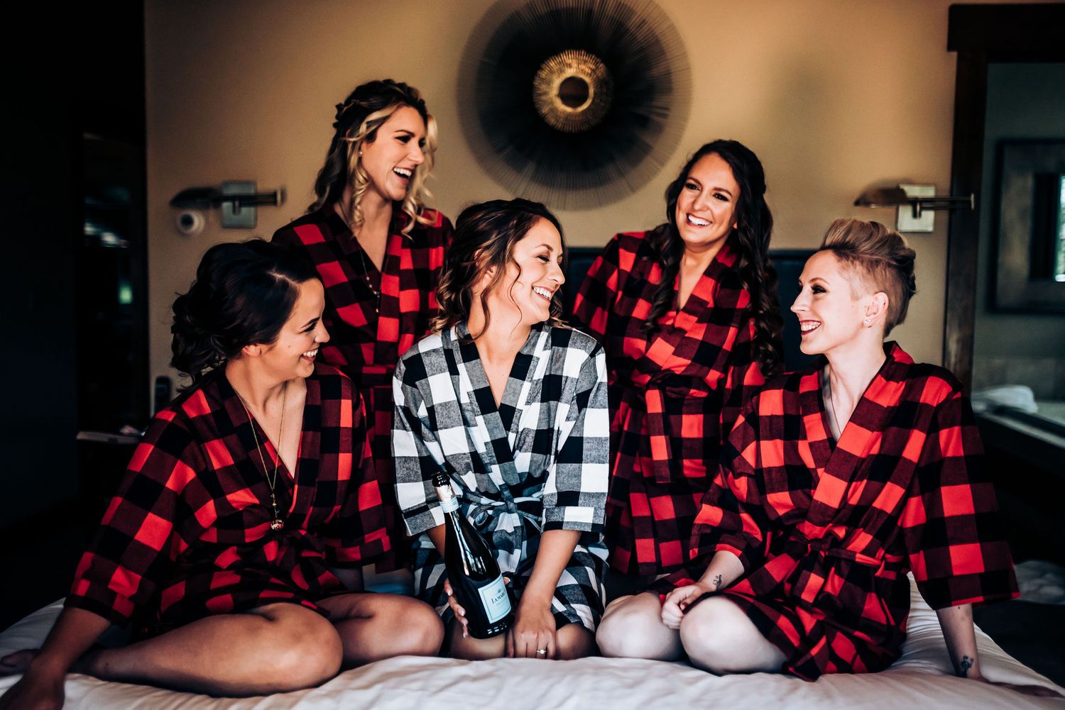 Wedding party lounging together wearing matching red and black buffalo plaid robes.