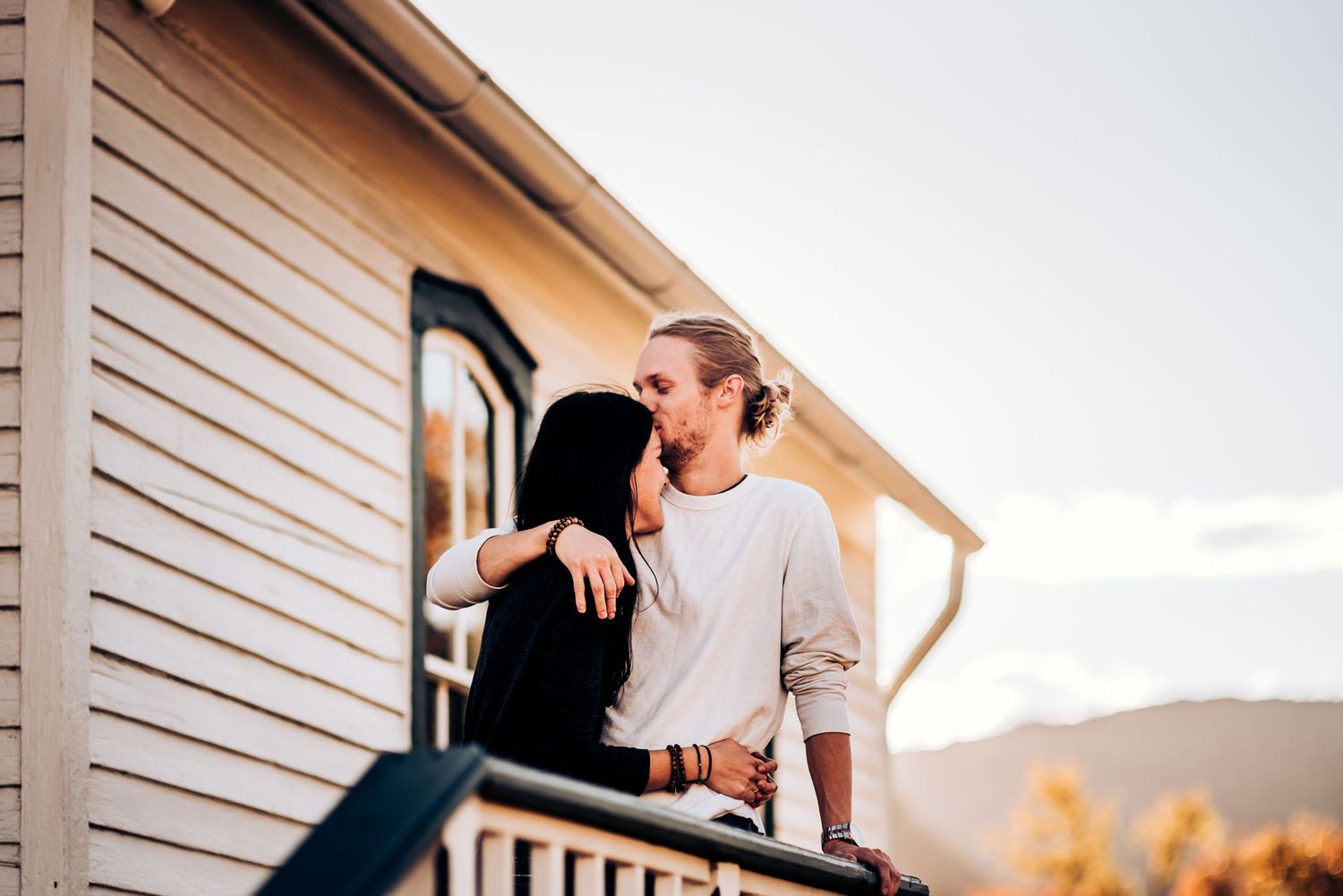 A couple embraces on a porch railing at sunset with mountains in the background.