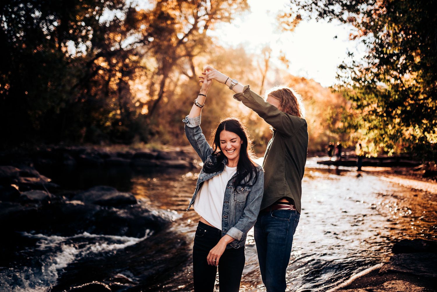 Happy couple dancing outdoors by a rocky riverbank in autumn.