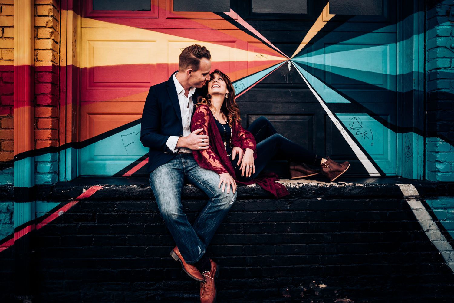 Two people sit together in a colorfully lit tunnel with geometric patterns on the walls.