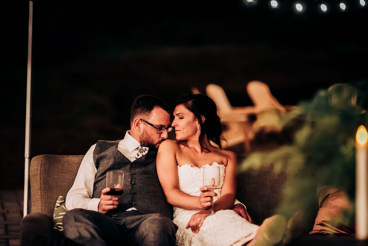 Intimate moment shared between couple during romantic evening reception with string lights overhead.
