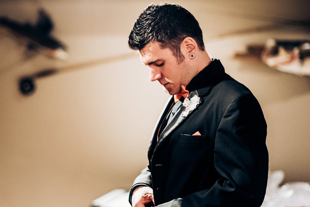 A groom in a black tuxedo adjusting his attire before the ceremony.