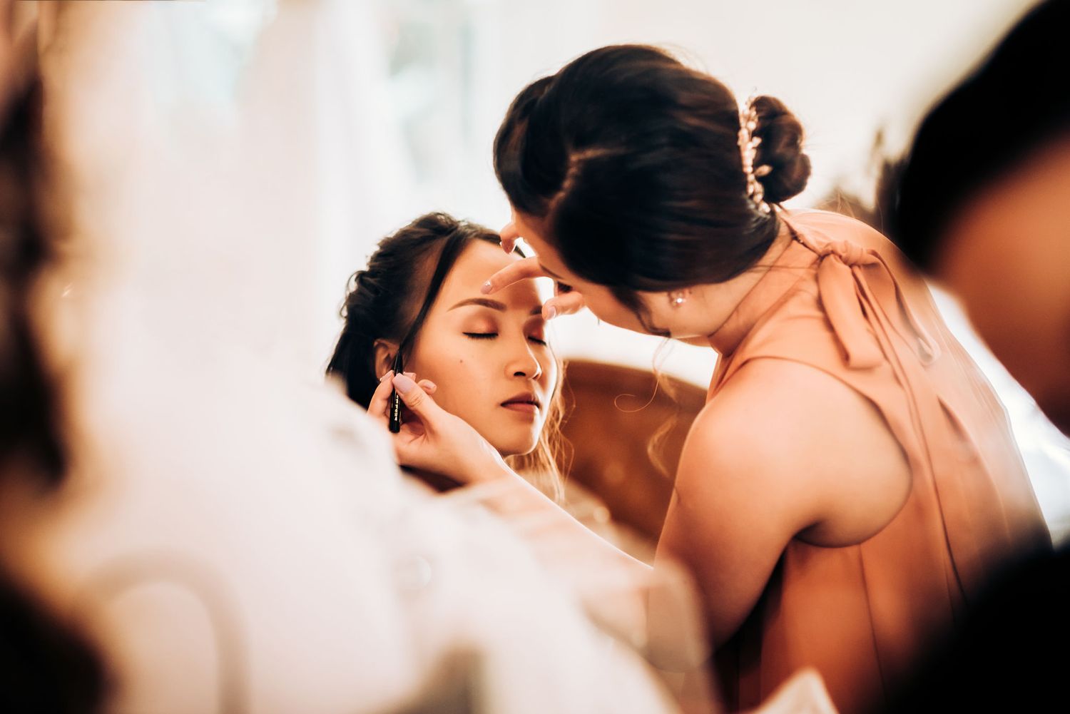 A behind-the-scenes moment of wedding day makeup application in warm lighting.