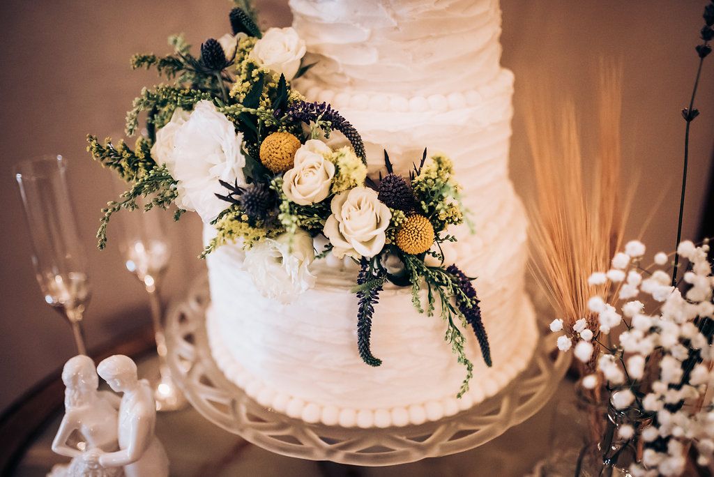 White tiered wedding cake decorated with fresh yellow and cream roses and greenery.