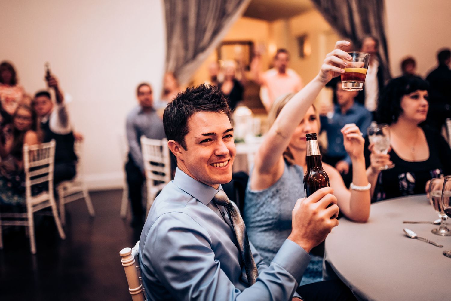Reception guest raises glass during celebration in elegant venue setting.
