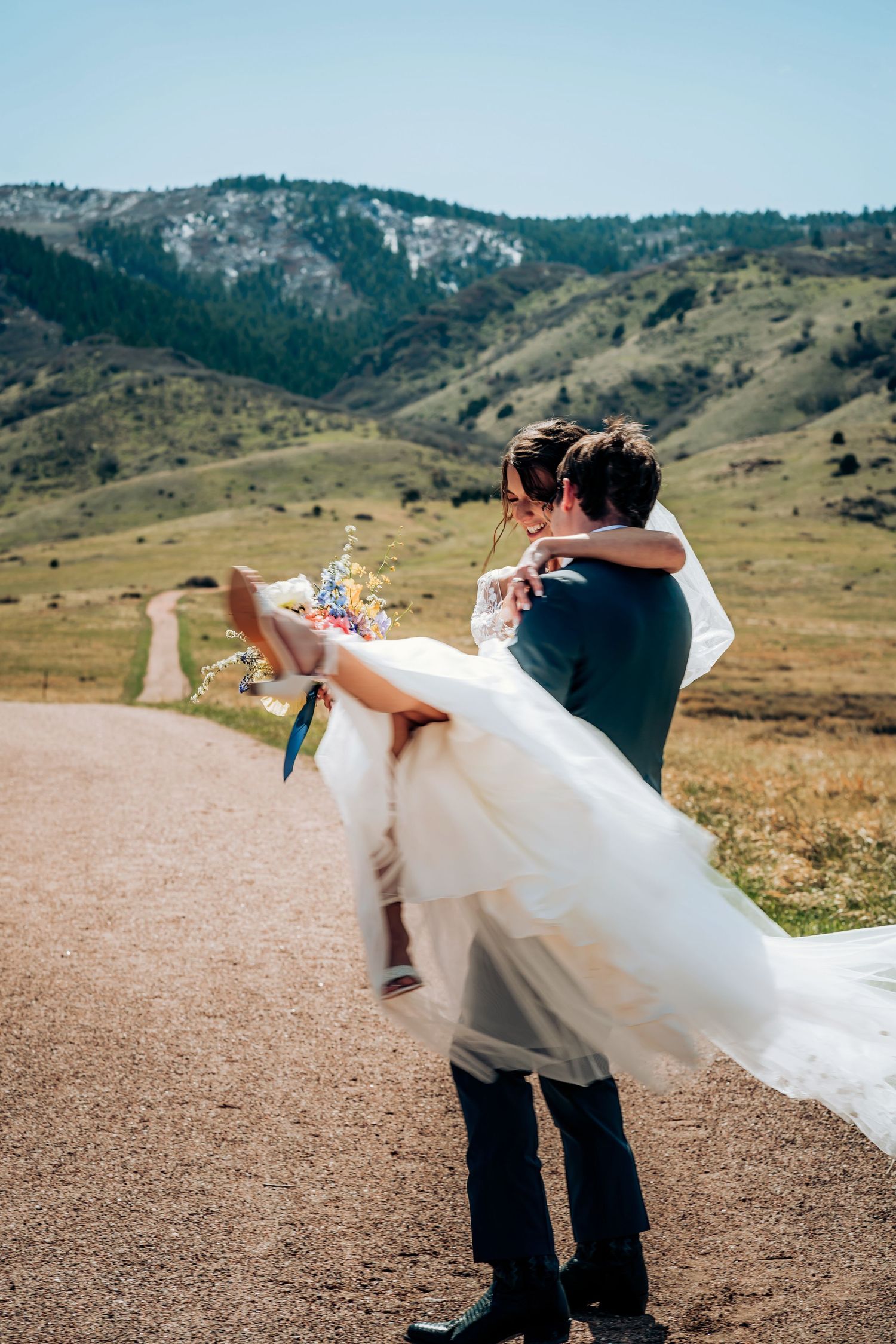 Couple spins playfully on a mountain overlook with flowing white wedding dress.