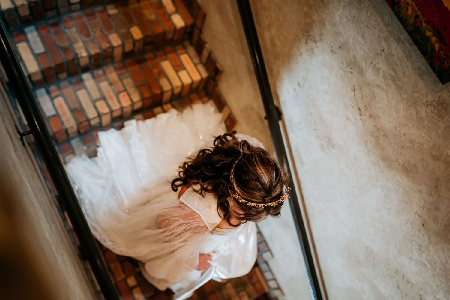 A bride in a white wedding dress walks down a staircase with dramatic lighting and shadows.