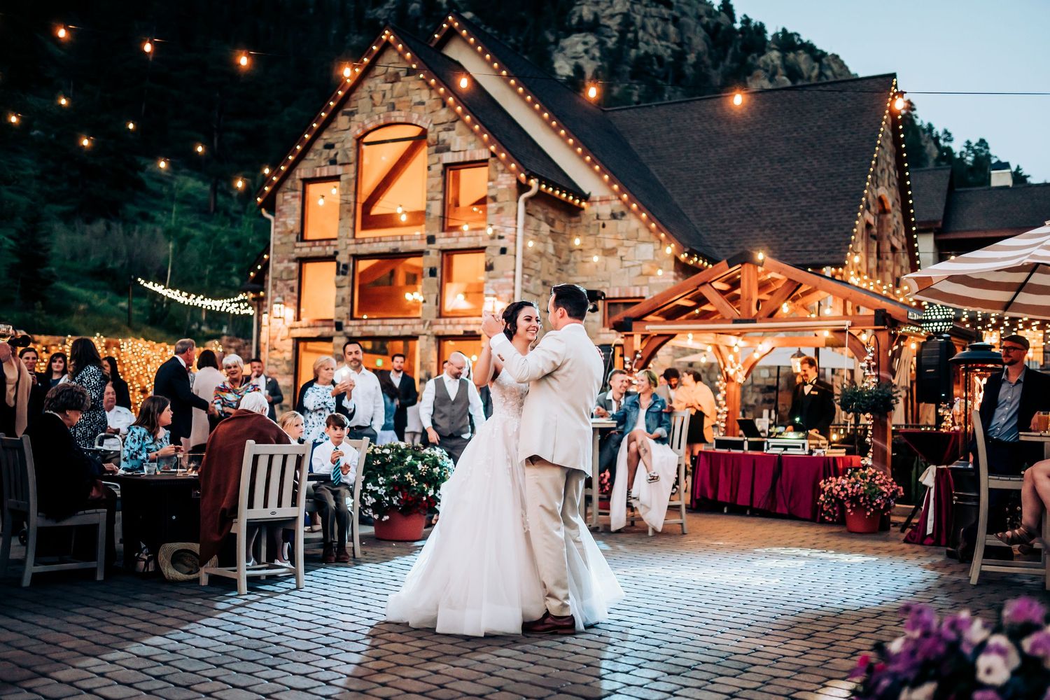 A rustic log cabin venue glows with string lights during an evening wedding reception.