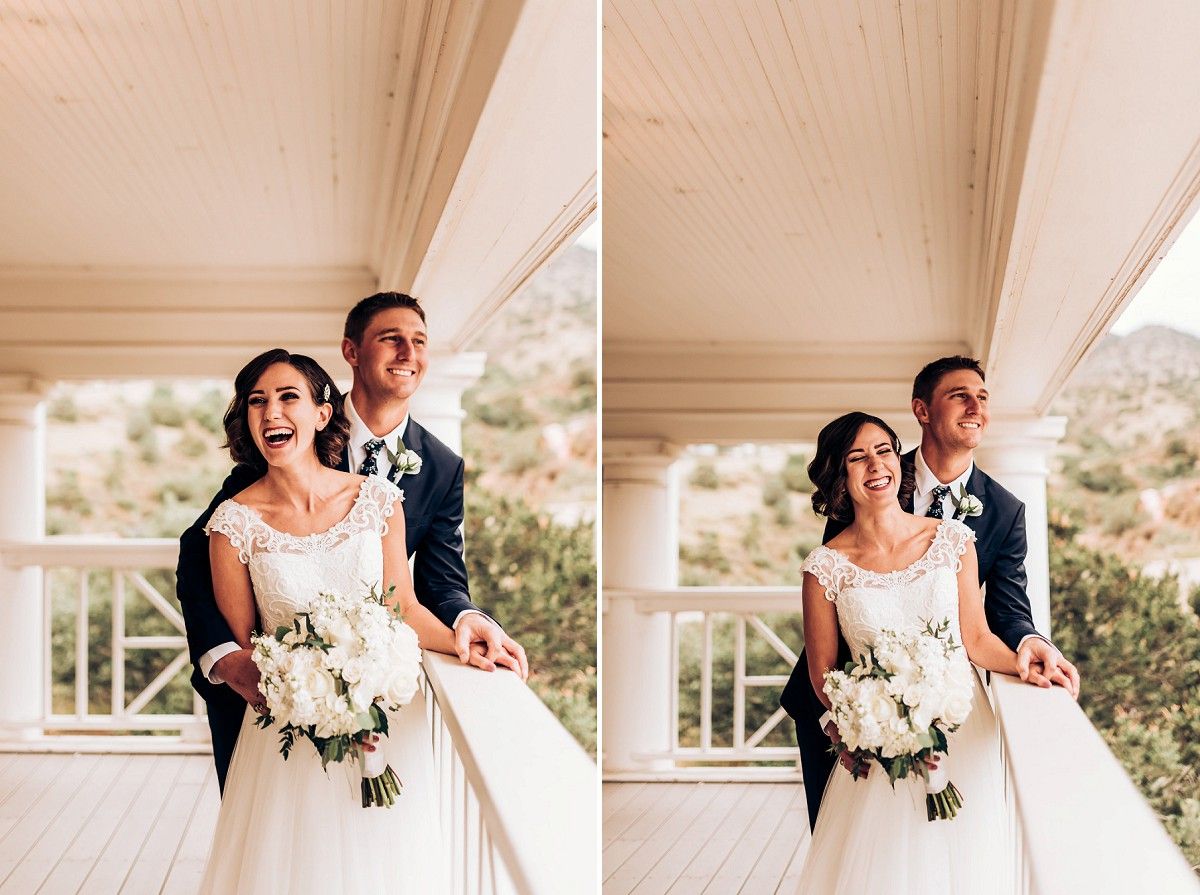 A newlywed couple poses on a white porch during their wedding photoshoot with a beautiful bouquet.