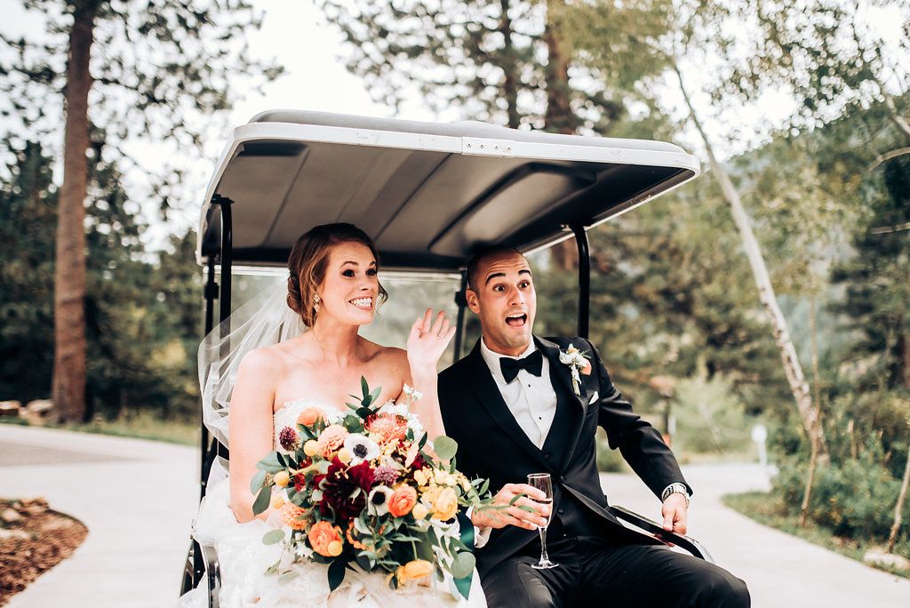 Newlyweds share a joyful moment while riding in a golf cart through a pine forest.