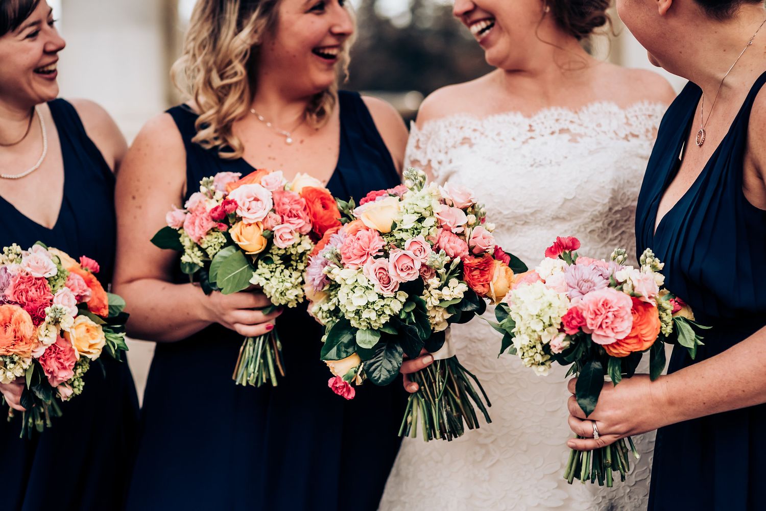 Close-up of bridesmaids holding vibrant pink and white flower bouquets in navy dresses.