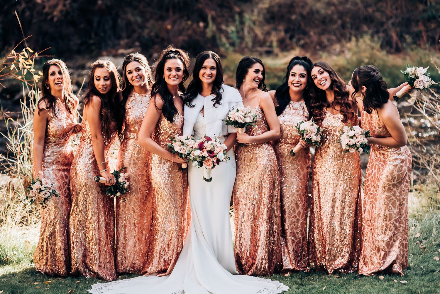 Bridesmaids wearing rose gold sequin dresses pose with bride in white gown against outdoor backdrop.