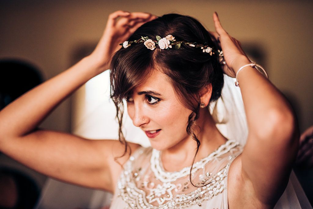 A floral crown adorns an elegant bridal hairstyle with lace dress detail visible.