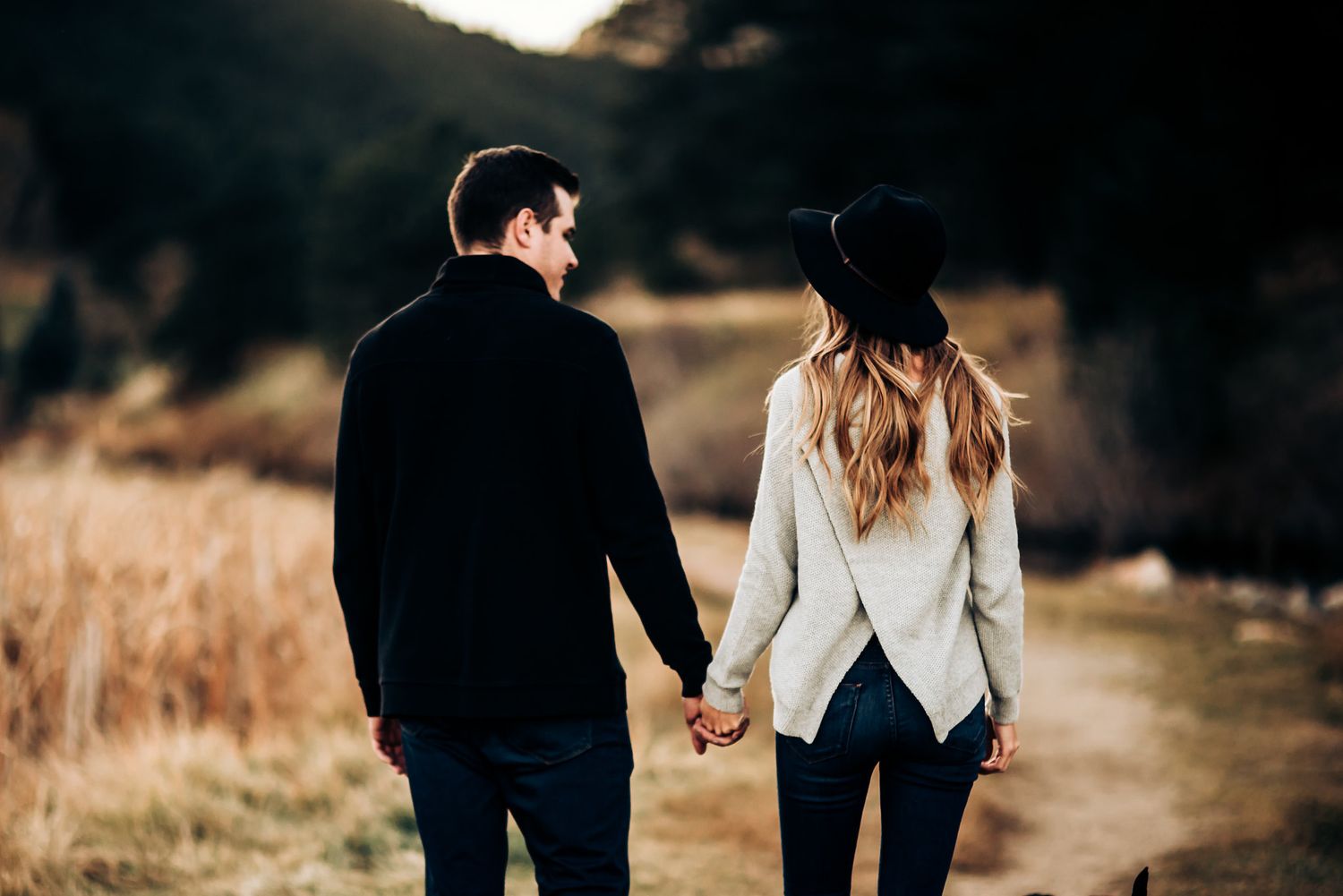 Couple holding hands while walking on trail at sunset.