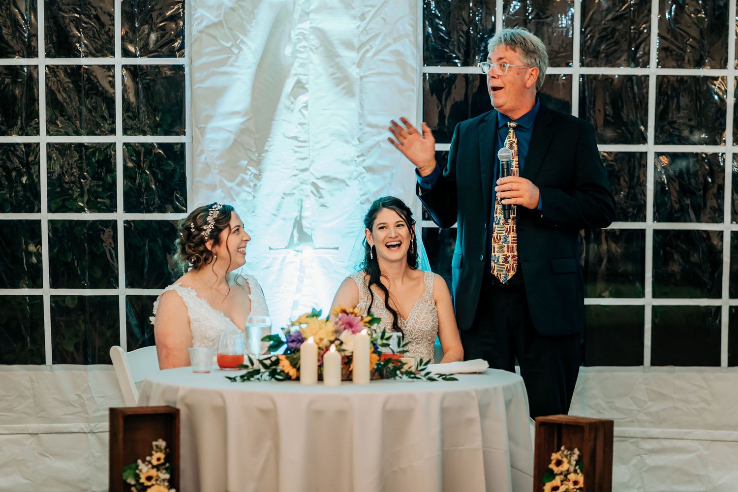 Speaker addressing guests during wedding reception in decorated indoor venue.