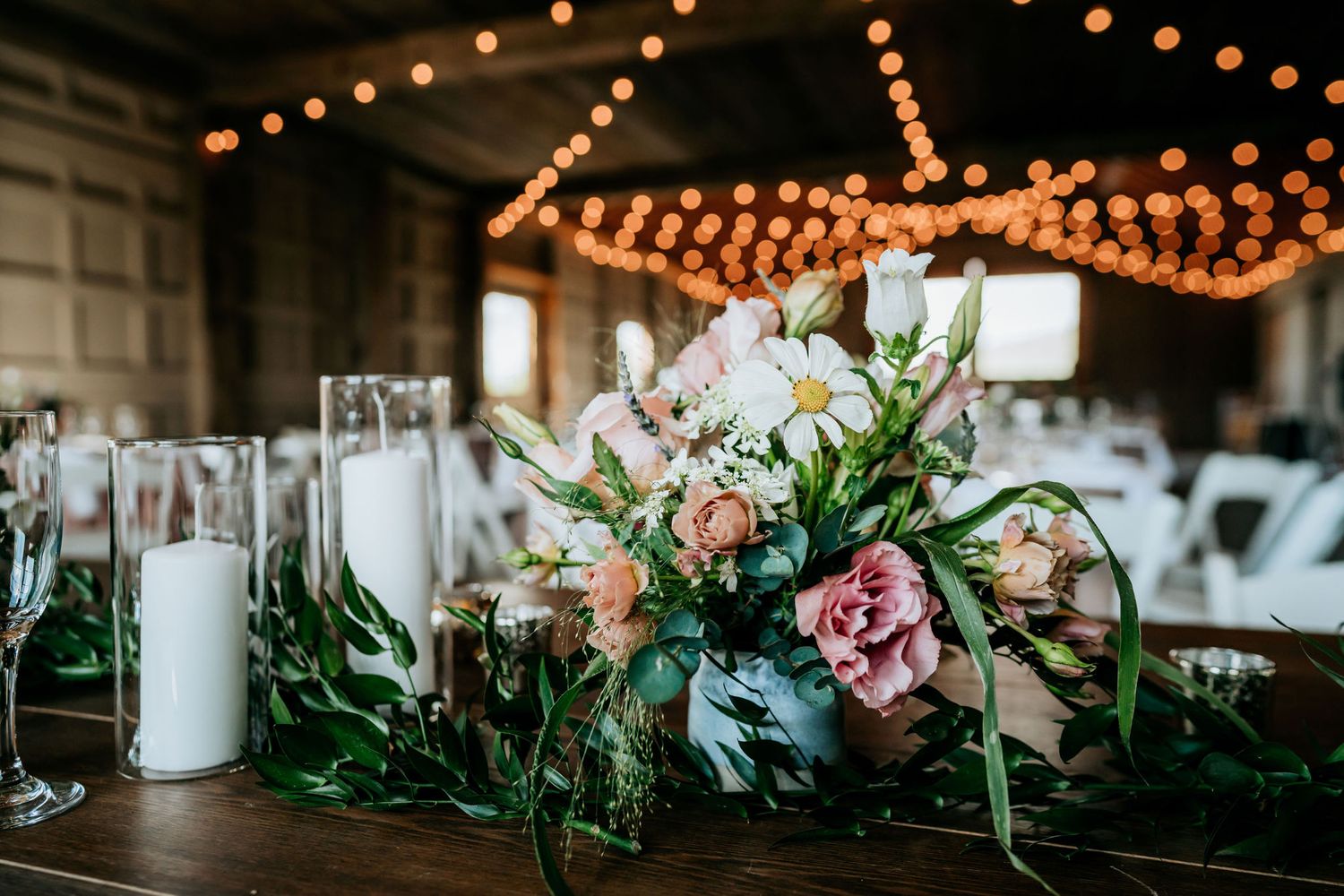 Rustic wedding table centerpiece with pink flowers and candles under string lights.
