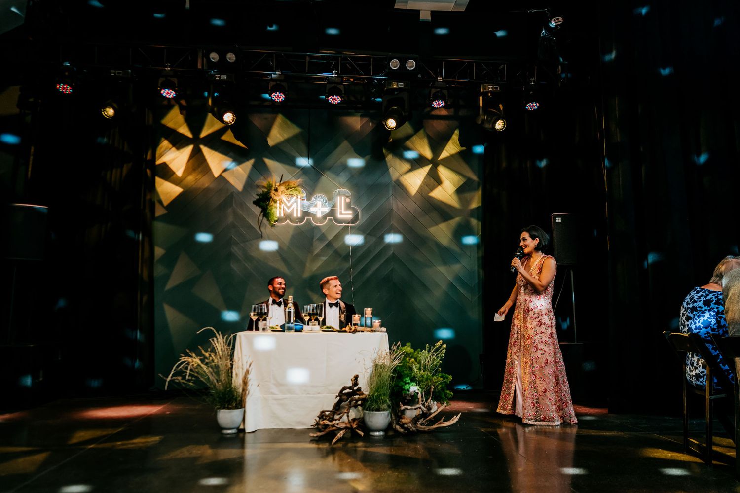 Event space with geometric backdrop, white table setting and decorative plants on stage.