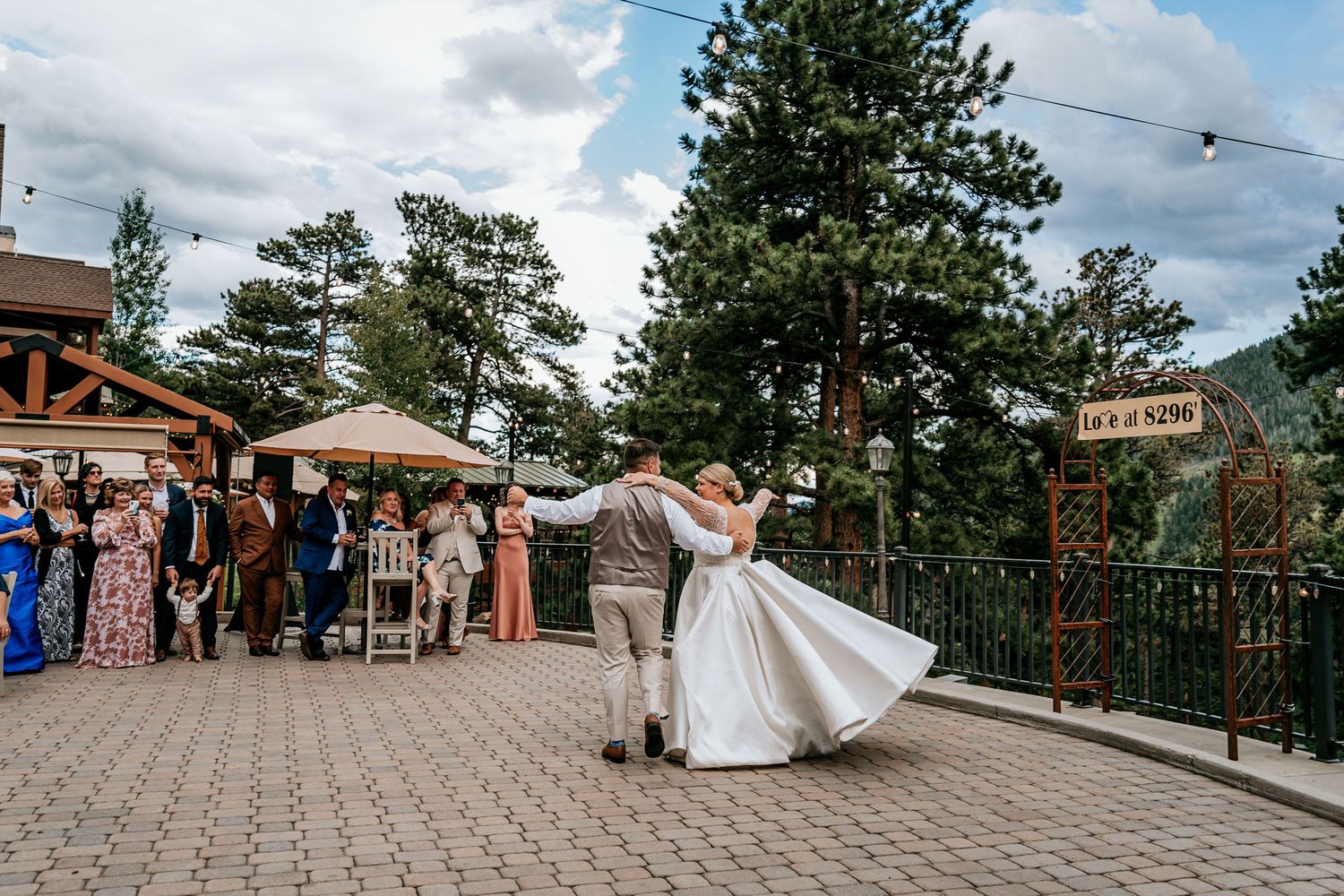 Couple sharing first dance on outdoor patio with wedding guests looking on.