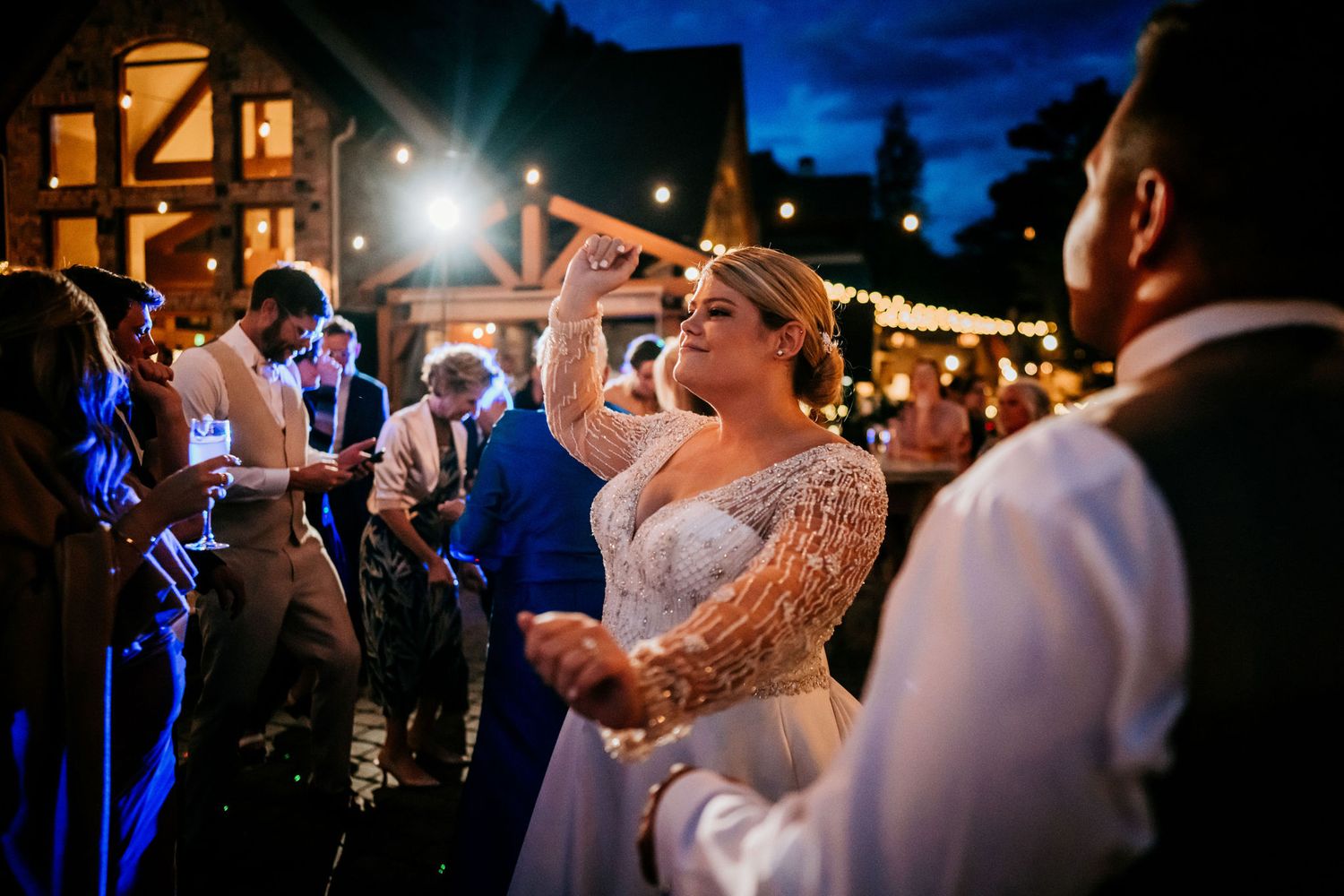 Wedding celebration dance party at night under outdoor string lights.