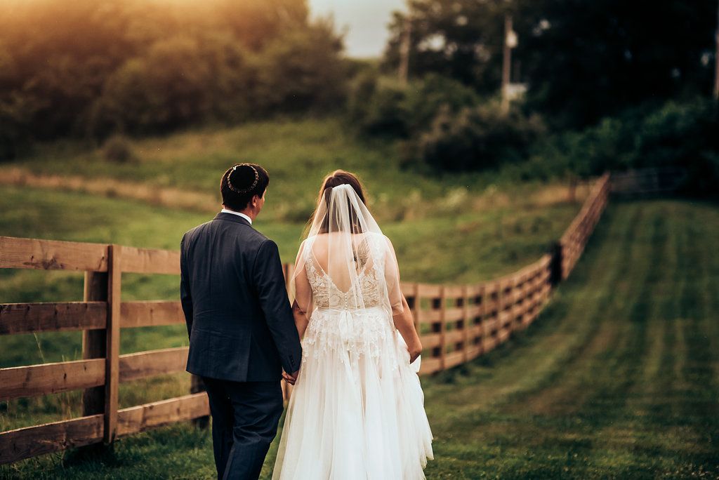 Couple walking along rustic wooden fence at sunset on rolling countryside hills.
