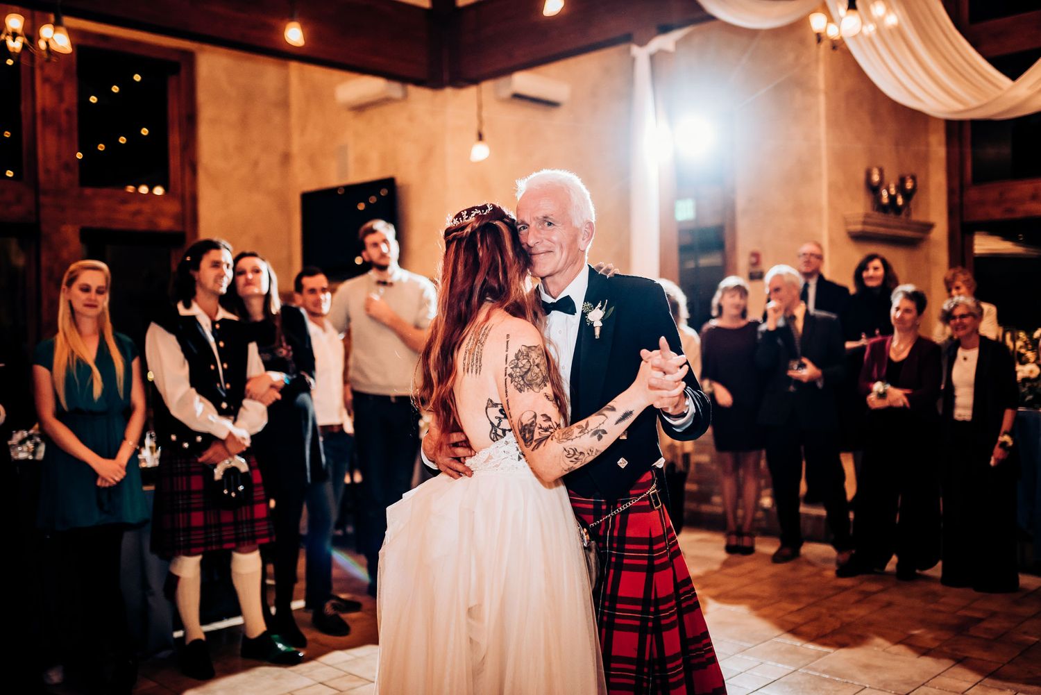 Traditional Scottish wedding dance with kilted guests watching in rustic venue.