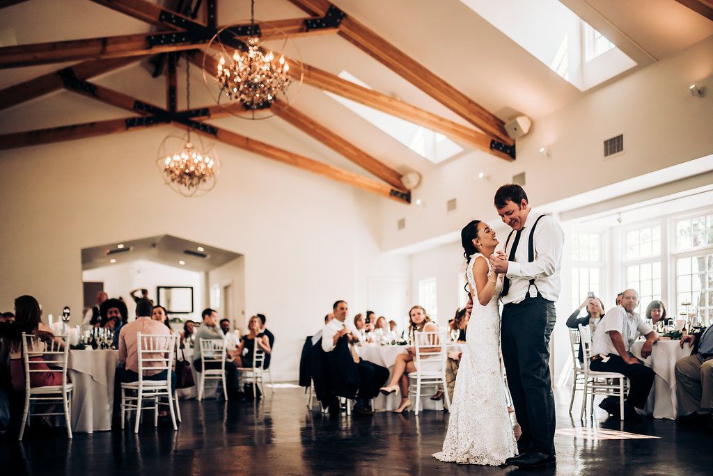 A first dance celebration in a spacious reception venue with wooden beams and chandelier lighting.