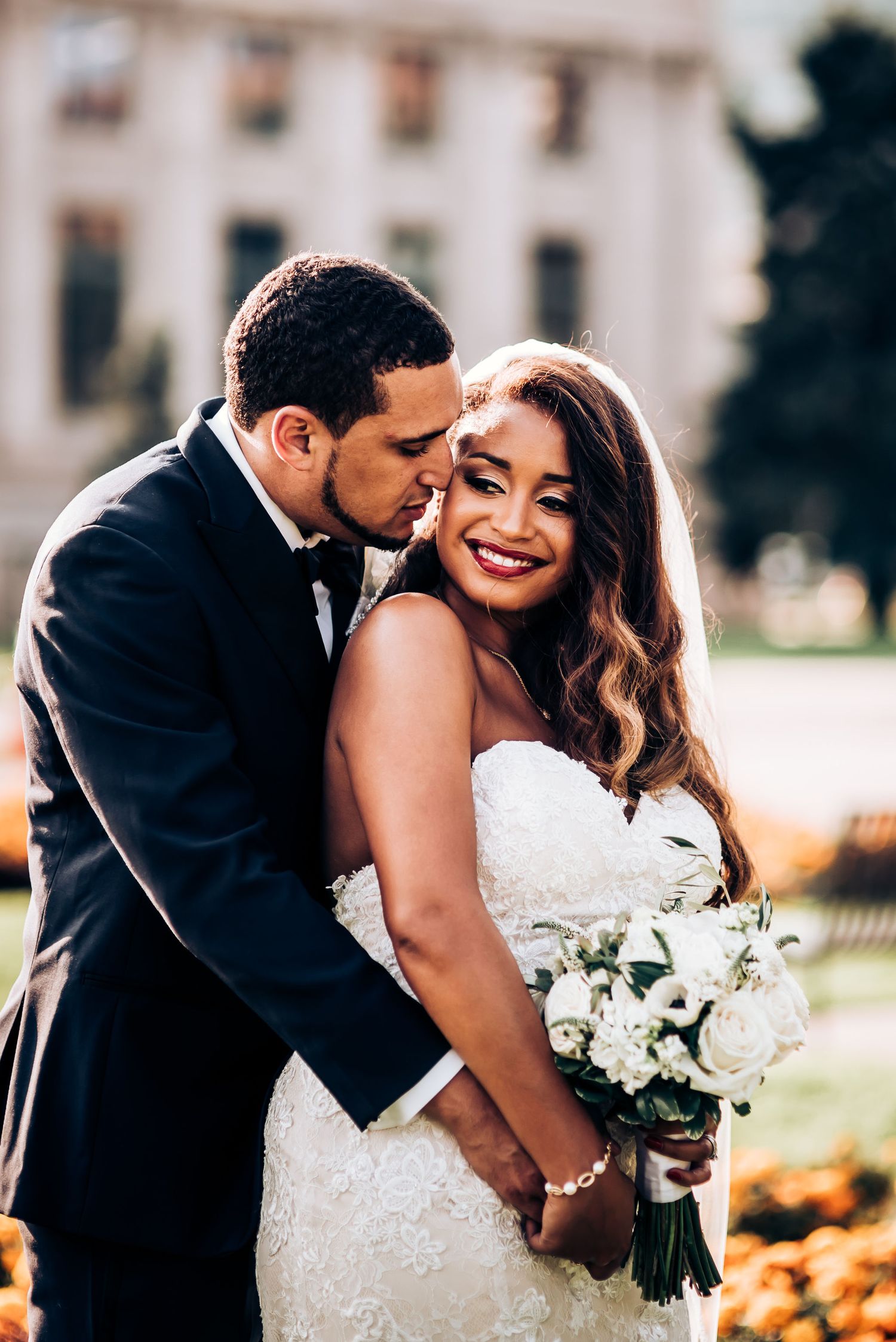 An intimate candid moment between newlyweds as they embrace outdoors with a white flower bouquet.