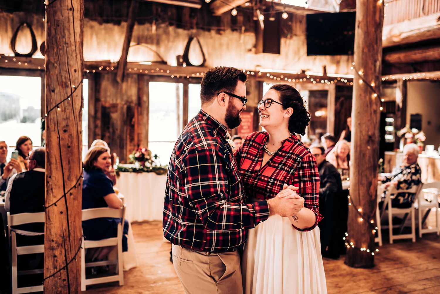 A couple in coordinated plaid outfits dancing together in a rustic wooden event space.