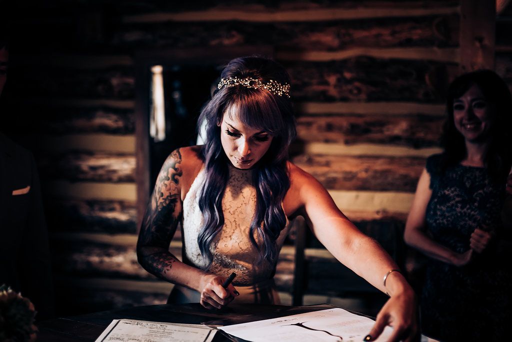 A wedding guest signs documents inside a rustic wooden cabin with warm lighting.