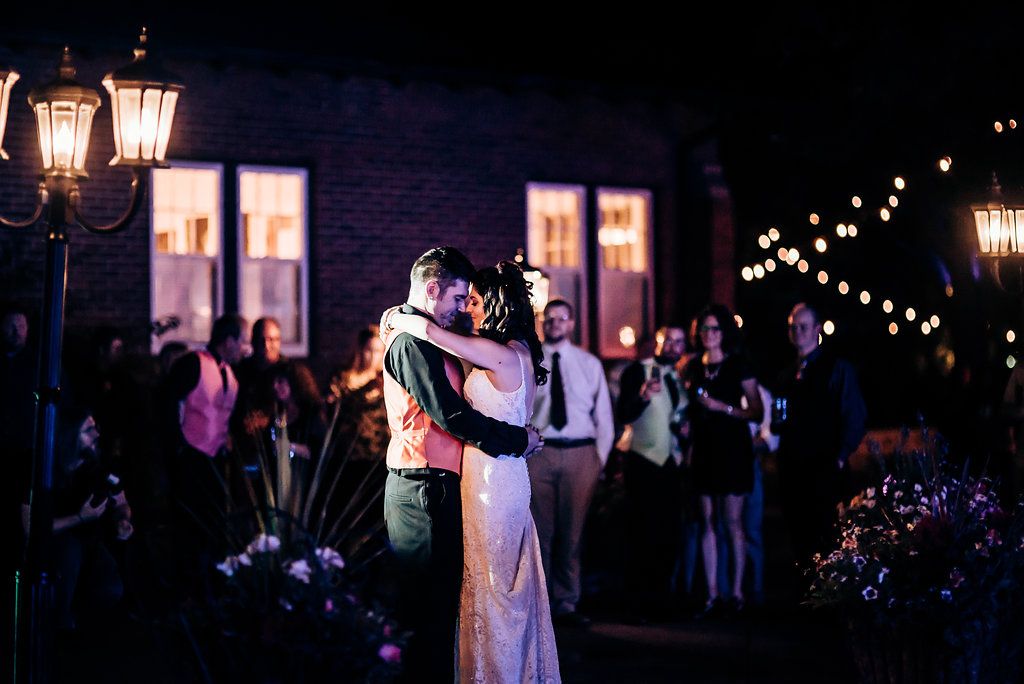 Couple embracing during their first dance at night with lantern lighting and guests watching.