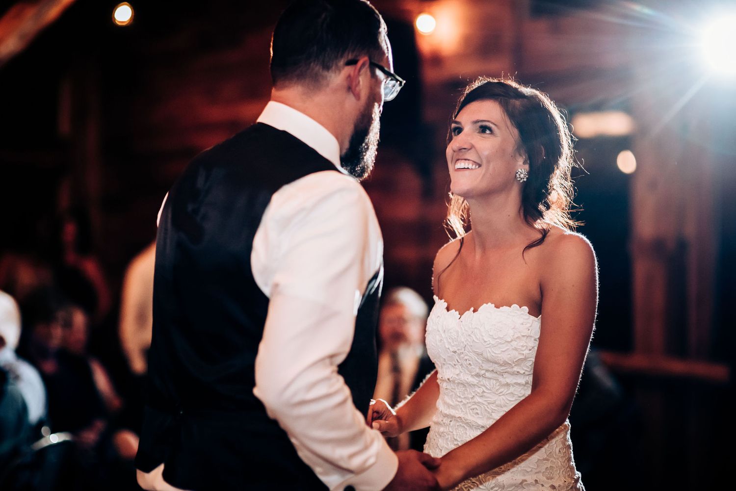 A romantic first dance moment captured in a rustic barn reception venue with glowing lights.