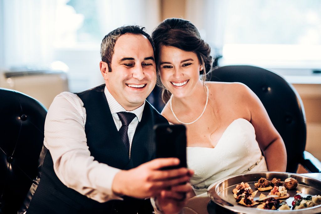 Wedding couple sharing a moment while looking at phone during reception.